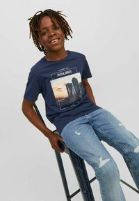 Mørkeblå bomulls t-skjorte med et urbant grafisk trykk, kombinert med lys blå slitte denimjeans med synlige hull og frynsete kanter.