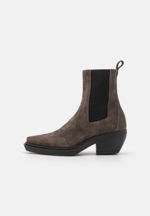 Bottine en daim marron avec panneau latéral élastique noir, languette à l'arrière et petit talon bloc incliné sur fond blanc.