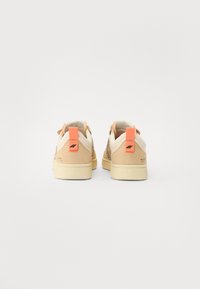 Beige sneakers med teksturert cheetahmønster, oransje hælfliker og subtil logo-detalj. Gummisåler og kontrasterende kremfargede detaljer.