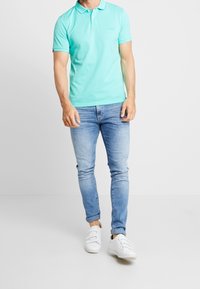 Polo vert menthe, à manches courtes, avec un léger brillant ; assorti à un jean en denim bleu clair et à des baskets blanches.