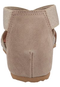 Bakvy av beige mockasinsandaler med justerbart elastiskt ankelsnöre och texturerad gummisula.