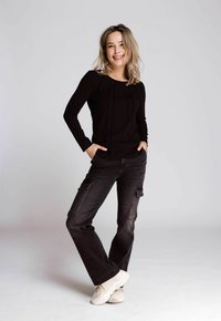 Schwarz langärmliges Oberteil mit strukturierten Nähten, kombiniert mit dunklen Cargo-Hosen mit Taschen, getragen mit hellen Sneakers vor einem neutralen Hintergrund.