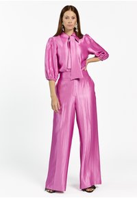 Pink satin blouse with a tie neck, puffed sleeves, and high-waisted wide-leg trousers. Features a smooth texture and shiny finish.
