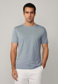 T-shirt s krátkým rukávem a kulatým výstřihem ve světle modré barvě s vodorovnými pruhy. Vyroben z měkké tkaniny, s jemným logem blízko lemování.