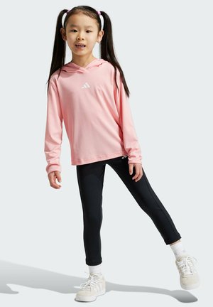 Light pink long-sleeve hoodie with a white logo, paired with black leggings and white sneakers. Smooth fabric with a relaxed fit.