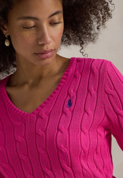 Πουλόβερ με V-λαιμόκοψη σε έντονο ροζ χρώμα, με σχέδιο πλέξης καλώδιο και ριμπ τελείωμα. Μικρό μπλε κεντημένο λογότυπο στο αριστερό μέρος του στήθους.