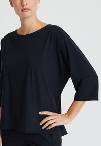Schwarzes, locker sitzendes Oberteil mit rundem Ausschnitt und 3/4-Ärmeln. Die glatte Textur, der weiche Stoff und das nahtlose Design steigern den Komfort.