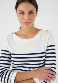 Marineblau und weiß gestreiftes Langarmshirt mit rundem Halsausschnitt und goldenen Knopf-Details auf der Schulter. Weicher Stoff mit Ärmeln in mittlerer Länge.