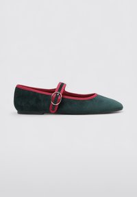Bailarinas de ante verde con punta afilada, que cuentan con una correa roja y un detalle de hebilla, complementadas por un borde rojo en contraste alrededor de la apertura.