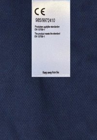 Marinblått tyg med en texturerad yta har en inifrån sydd skötselmanual som visar CE-märkning och brandsäkerhetsvarning.