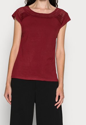 Haut bordeaux à manches courtes avec des détails texturés sur les épaules, en tissu doux et avec un col rond classique. Associé à un pantalon noir ample.