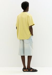 Žluté oversized tričko, světlé denimové šortky, černé sandály. Jednoduchý design s krátkými rukávy a bočními kapsami na šortkách.
