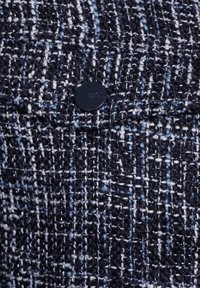 Tissu texturé dans des nuances de bleu marine et blanc, présentant un motif tissé avec des accents bleu clair, fixé par un bouton bleu foncé.