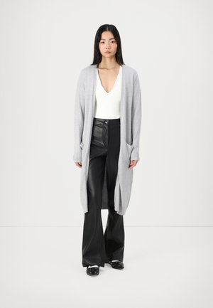 Light gray long cardigan made of a soft knit material, featuring ribbed cuffs and pockets. Paired with fitted black leather pants and clogs.