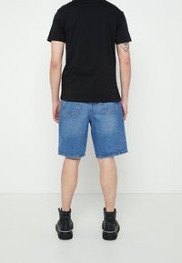 Mustat lyhyet hihaisat paidat yhdistetty sinisiin farkkushortseihin. Shortseissa on klassinen leikkaus ja takataskut; yhdistetty mustiin kenkiin.