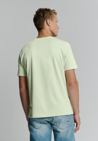 Lichtgroene T-shirt met korte mouwen en een ronde hals. Zachte katoenen stof. Casual pasvorm, effen achterkant, gecombineerd met lichtblauwe spijkerbroek.