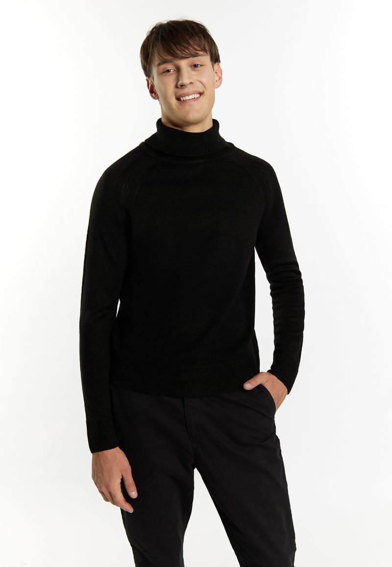 Schwarzer Rollkragenpullover aus weichem Strickmaterial mit langen Ärmeln, gerippten Bündchen und Saum, getragen mit dunklen Hosen, vor einem weißen Hintergrund präsentiert.