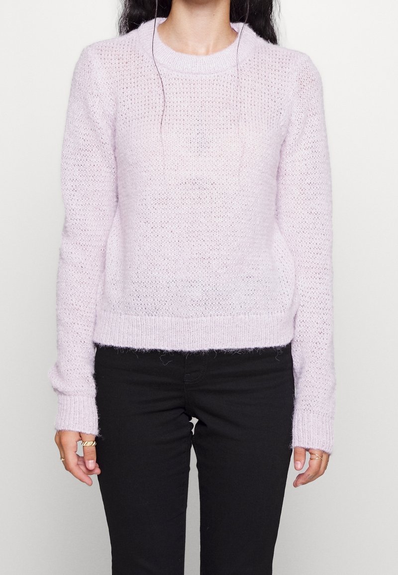 Pull en tricot lavande avec tissu texturé, encolure ronde et poignets côtelés, associé à un pantalon noir. Apparence douce et duveteuse.