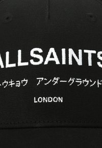 Black cap with white embroidered text reading "ALLSAINTS" and additional characters, plus "LONDON" at the bottom. Smooth fabric texture.