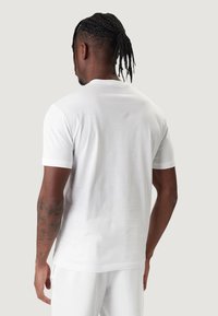 Maglietta bianca in cotone con maniche corte, scollo rotondo, trama liscia e design semplice, vista da dietro. Senza motivi o accenti.