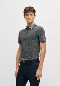 Polo shirt grigio scuro con un motivo a trama, maniche corte e colletto a contrasto. Abbinato a pantaloni blu navy e una cintura nera.