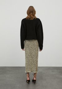 Zwarte textuur crop sweater over een midi rok met luipaardprint. De outfit bevat hoge hakken met enkelbandjes.