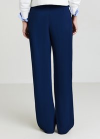 Marineblaue, weitläufige Hosen aus glattem Stoff. Mit hohem Bund und klaren Linien, ohne sichtbare Beschläge oder Verzierungen.