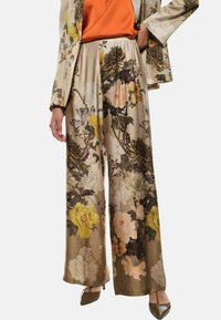 Pantaloni a gamba larga floreali in un tessuto setoso, con grandi fiori gialli e rosa pallido su uno sfondo beige, dotati di vita elastica.