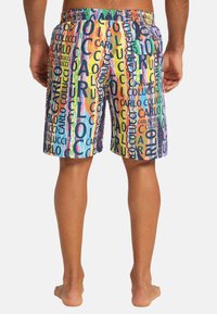 Bunte Schwimmshorts mit einem lebhaften, wiederholten "CARLO COLUCCI" Textmuster in Blau, Orange, Gelb und Grün auf einem gemusterten Hintergrund.