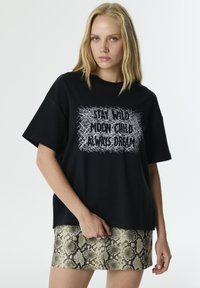 Camiseta de algodón negra con mangas cortas, que presenta un diseño gráfico de texto en blanco. Combinada con una falda corta de mini con estampado de serpiente texturizado.