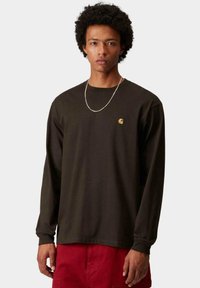 Camicia a maniche lunghe in cotone marrone scuro, con un piccolo logo giallo sul petto e un fit rilassato. Design semplice senza fantasie.