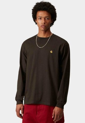 Camisa de manga larga de algodón marrón oscuro, con un pequeño logo amarillo en el pecho y un corte relajado. Diseño simple sin patrones.