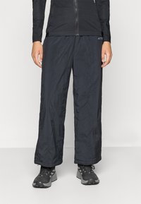 Črne, lahke, vodoodporne hlače ohlapnega kroja z elastiko v pasu; imajo subtilno teksturo in podrobnost z logotipom blizu pasu.