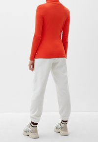 Oranje lange mouwen turtleneck shirt, gecombineerd met witte textuur jogger broeken en beige sneakers met zwart-witte accenten.