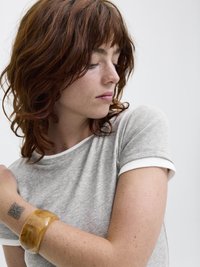 Gray t-shirt with white trim, worn with a glossy, amber-colored bangle on a freckled arm. Focus on texture and color contrast.