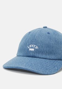 Boné de denim azul com aba curva, apresentando um logotipo "LEVI'S" bordado em branco e uma superfície de tecido texturizado. Estrangulador ajustável na parte de trás.