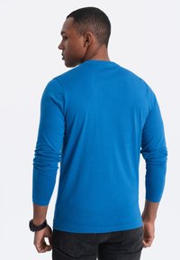 Blauwe longsleeve shirt van gladde stof, met een ronde hals en aansluitende mouwen. Draagt iemand die van achteren is gezien.