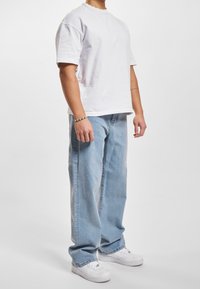 Camiseta de algodón blanca de manga corta, combinada con unos vaqueros de mezclilla azul claros. Zapatillas blancas completan el conjunto. Diseño simple y ajuste casual.