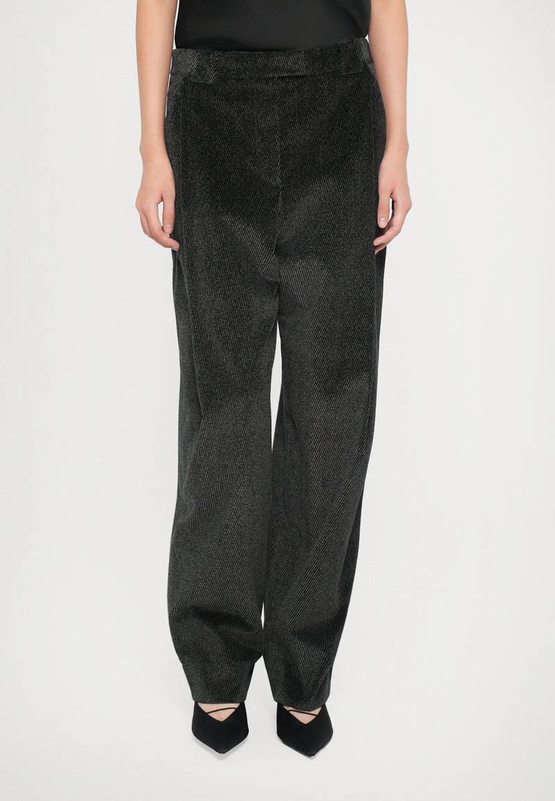Pantalon en velours côtelé noir à jambes larges et surface texturée, avec une taille haute et de subtiles rayures verticales.