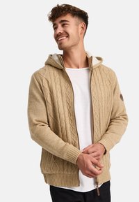 Cárdigan de punto beige con capucha, con diseño de patrón de trenza, cierre de cremallera, puños acanalados y un suave forro de forro polar.
