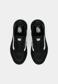 Svarte joggesko med en strukturert svart overdel, hvite sidestiper og svarte snøringer. Har rund tå og Vans-merke på tungen.