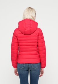 Κόκκινο επενδυμένο μπουφάν με κουκούλα, με ραμμένες τμήματα, ελαστικές μανσέτες και εφαρμοστή γραμμή, συνδυασμένο με μπλε τζιν.