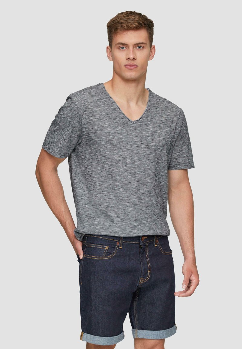 Szary t-shirt z krótkim rękawem w serek, wykonany z teksturowanej tkaniny, w zestawieniu z ciemnymi szortami dżinsowymi z podwiniętymi mankietami i widocznym przeszyciem.