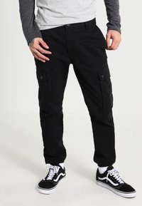 Svarta cargobyxor med sidofickor, rak passform och ett hållbart tyg. Bärs med svarta och vita sneakers för en avslappnad look.