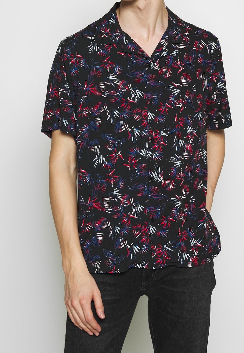 Camisetta a maniche corte in tessuto nero con un motivo di foglie di palma multicolore nei toni del rosso, blu e bianco. Vestibilità comoda con colletto a punta.