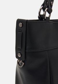 Černá kožená kabelka s hladkým povrchem, vybavená stříbrnými detaily, popruhem s kroužky a strukturovaným designem.