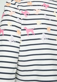 Gestreiftes Langarmoberteil in Marineblau und Weiß, verziert mit verspielten Hundefiguren in Rosa und hellen Farbtönen auf dem Stoff.