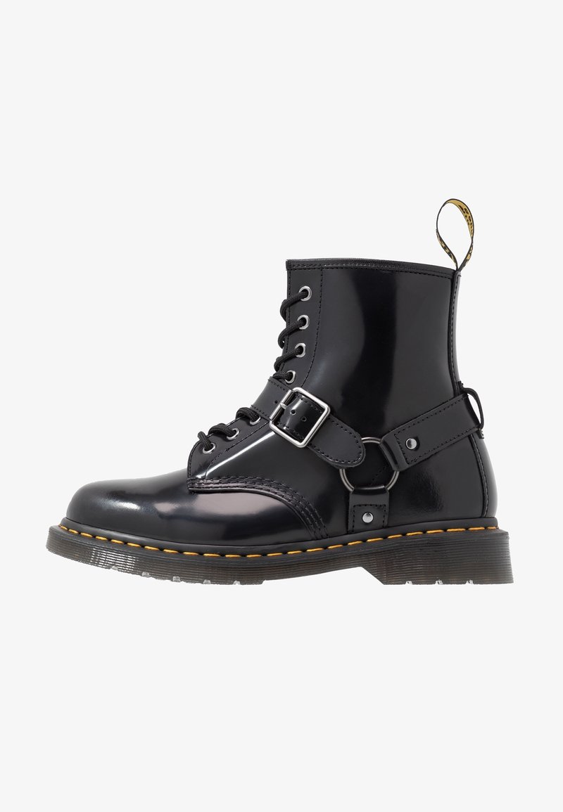 Botte noire en cuir brillant à lacets avec sangle à boucle, couture jaune le long de la semelle et languette à l'arrière.