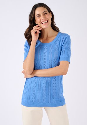 Maglietta a maniche corte di maglia azzurro chiaro con un motivo a diamante testurizzato, scollo a barca e orlo a costine. Indossata con pantaloni chiari.