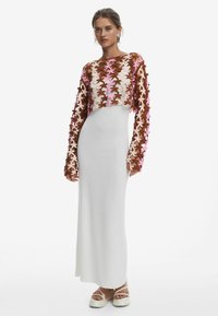 Robe longue blanche avec un corsage ajusté et une jupe évasée, dotée d'une superposition courte brodée de fleurs marron et rose et de manches longues.